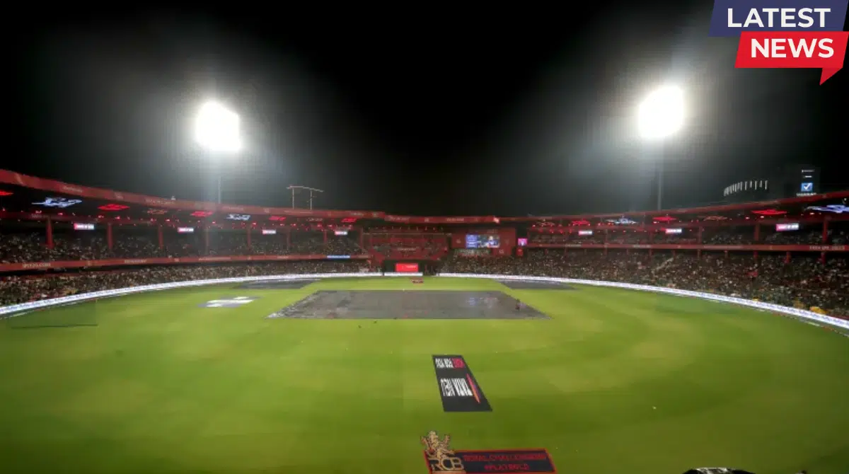 Rain cover placed over the pitch at M. Chinnaswamy Stadium during a night match as floodlights illuminate the packed cricket stadium.