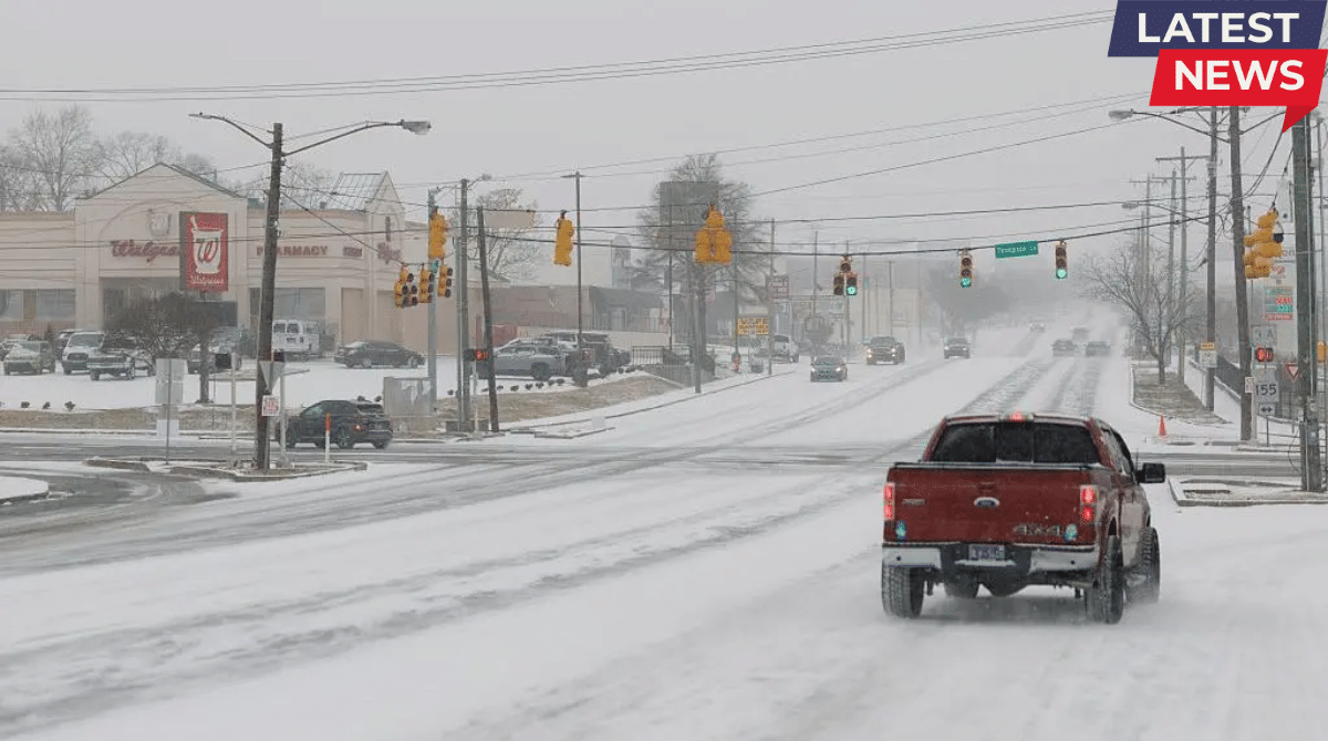 Snow-covered road with vehicles driving slowly during a winter snowstorm in a U.S. town as traffic lights glow through heavy snowfall.